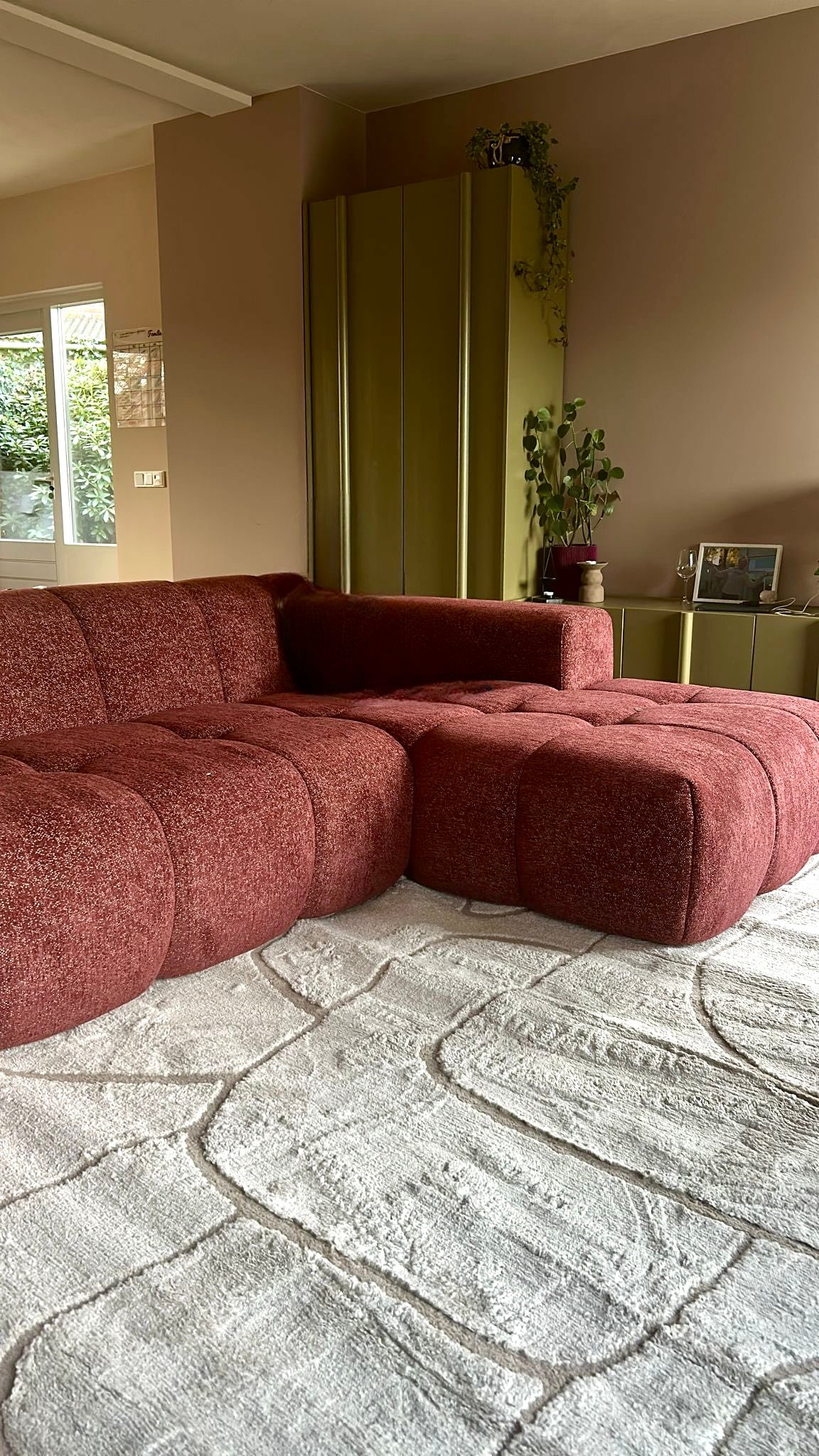 Woonkamer detail met bordeaux bouclésofa en olijfgroene kasten, Tilburg